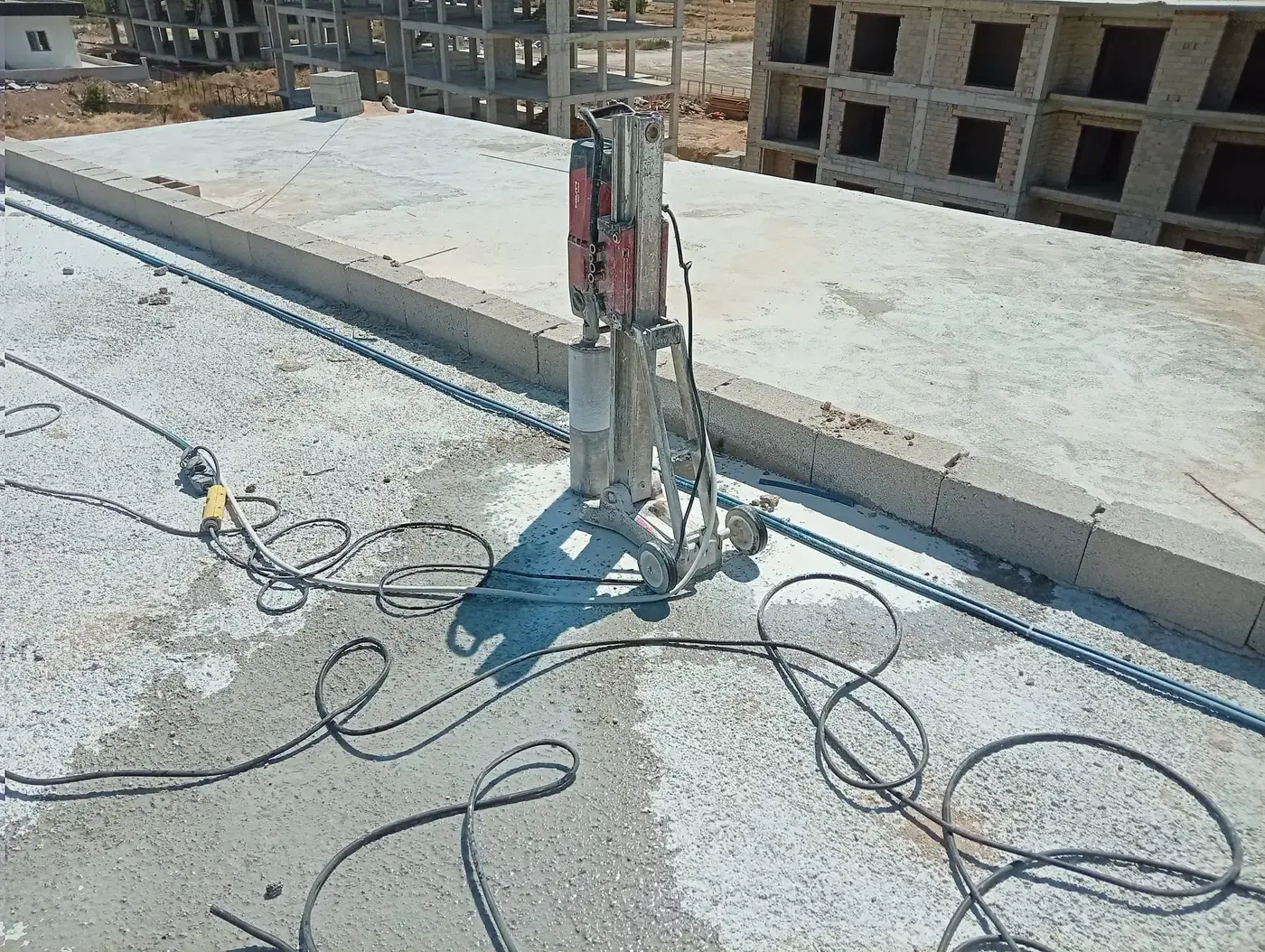 Yapım aşamasındaki binanın çatı döşemesinde parapet dibine kurulmuş sehpalı karot makinesi ve döşemede serili kablolar