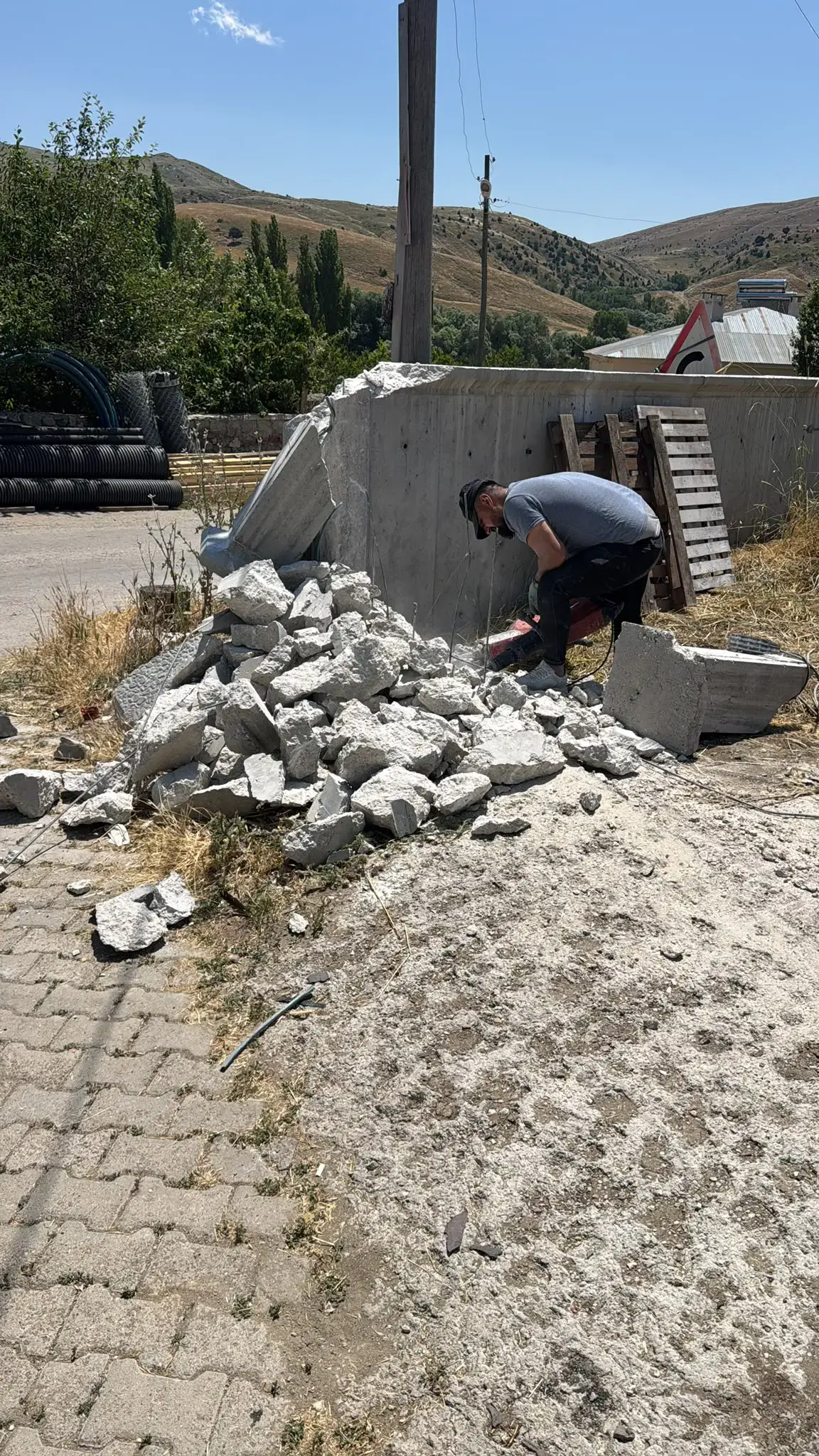 Kırıcıyla sökülen betonarme duvar, duvar dibinde toplanmış moloz yığını ve arkada kilit taşı kaplı alan