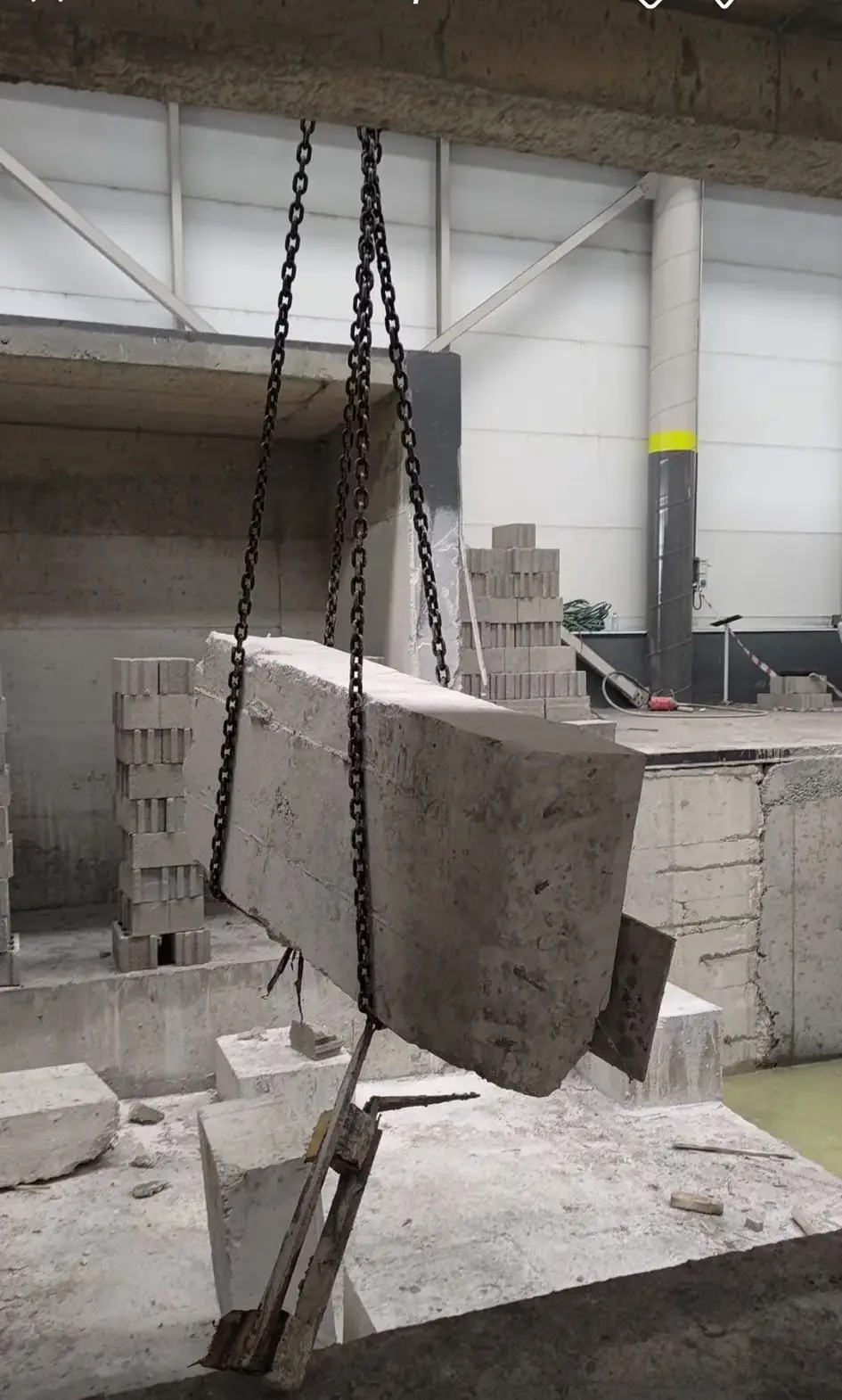 Zincir sapanla askıya alınmış büyük betonarme blok ve arkada briket istifleriyle desteklenmiş kesim alanı